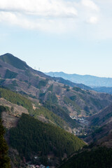 冬の関東地方の山々の風景。深い谷間にひっそりと佇む小さな集落（山里）と、幾重にも重なる山並み。日本の穏やかな田舎や、地方の暮らしをイメージさせる、郷愁を誘う景色。縦横両方の構図あり。

