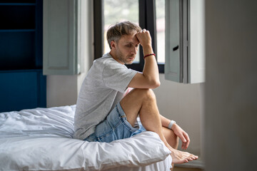 Thoughtful anxious middle aged man sadly sitting on bed worry about life troubles, difficult...
