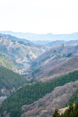 Naklejka premium 冬の関東地方の山々の風景。深い谷間にひっそりと佇む小さな集落（山里）と、幾重にも重なる山並み。日本の穏やかな田舎や、地方の暮らしをイメージさせる、郷愁を誘う景色。縦横両方の構図あり。