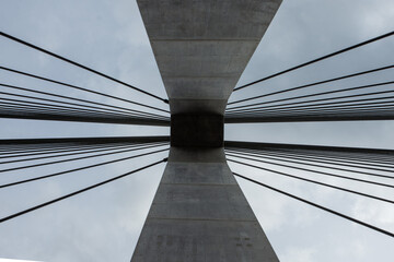 Fototapeta premium 埼玉県秩父市の合角漣大橋の橋脚を真下から見上げた、抽象的な建築写真。コンクリートの主塔から放射状に伸びるケーブルが作り出す、幾何学的で力強いデザイン。近代的な土木技術やインフラ、アートを象徴するイメージ。