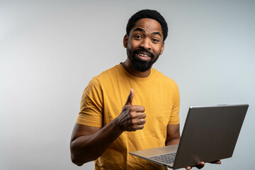 Smiling young Black man holding laptop and showing thumbs up, isolated on white background, symbolizing positive freelance experience