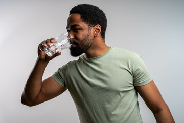 Young Black man drinking water from bottle, isolated on white background, promoting hydration,...