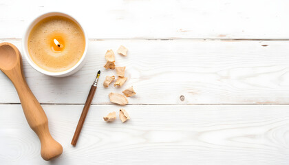 Aromatic candle in a white bowl surrounded by wooden spoon, pen, and scattered wood shavings on a rustic white wooden surface creating a serene atmosphere for relaxation