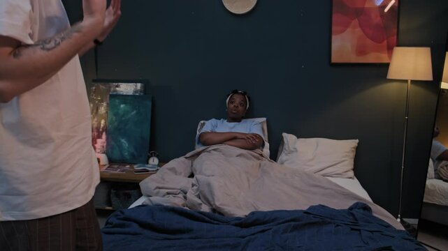 Unrecognizable man going back and forth in bedroom, nagging his Black wife while she lying in bed with arms crossed