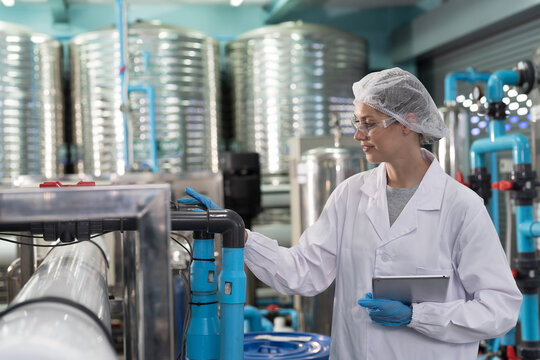 Drinking water manufacturers and production line. Water filter machine. Female worker inspecting quality of water filter machine and pipeline in drinking water production plant - Powered by Adobe