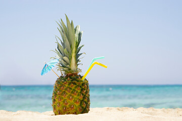 Ripe pineapples  cocktail with straw and umbrella on the sandy tropical beach background with copy space. Leisure in summer and Summer vacation concept.
