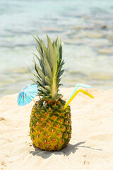 Ripe pineapples  cocktail with straw and pink umbrella on the sandy tropical beach background with copy space. Leisure in summer and Summer vacation concept. Vertical
