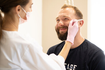 The cosmetologist marks with a pencil the points for beauty injections of botulinum therapy on the face of a man. Concept Plastic surgery and cosmetology for men with copy space