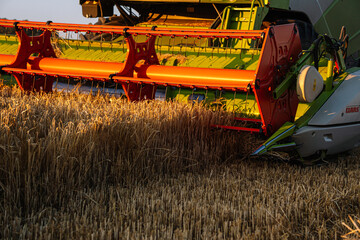 Close-up of combine harvester cutting barley crop with blades during sunset