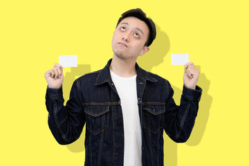 Young Man Holding Two Blank Cards, Yellow Background, Questioning Expression