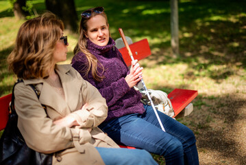 Visually impaired woman and her female friend sitting in a city park and talking