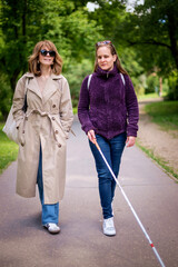 A visually impaired woman with white cane walking with her female friend in the city