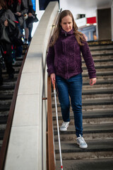 A visually impaired woman with white cane coming down the stairs outside