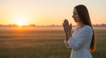 A woman is praying during sunrise in a golden field.
