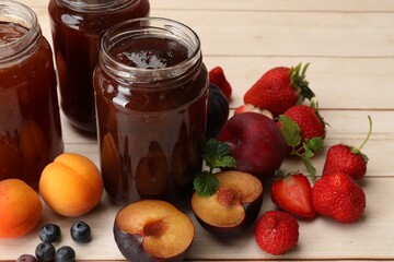 Different jams in jars and ingredients on white wooden table, closeup