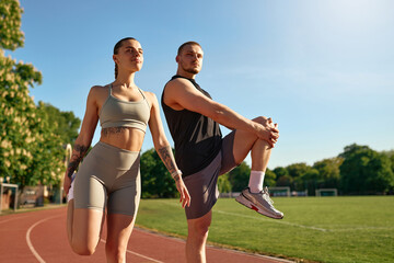 Sporty couple stretching together before workout on stadium track