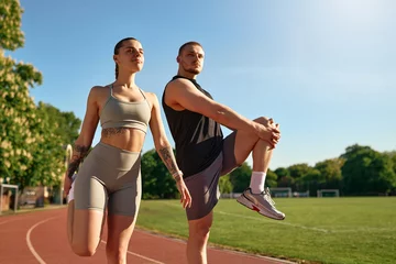 Fototapete Fitnessstudio Sporty couple stretching together before workout on stadium track  © Valerii Apetroaiei