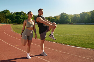 Sporty couple stretching together before workout on stadium track