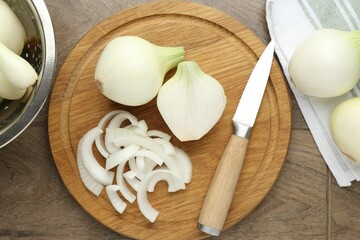 Cut ripe onions and knife on wooden table, flat lay