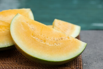 Pieces of ripe yellow watermelon on wicker table near swimming pool, closeup