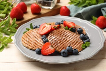 Tasty Dutch waffles (stroopwafels), mint and berries on light wooden table, closeup