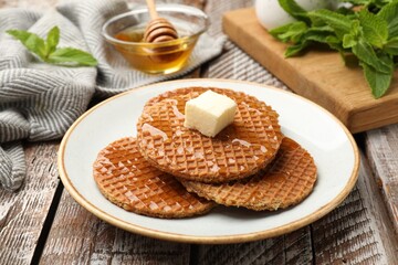 Tasty Dutch waffles (stroopwafels) with honey and butter cube on wooden table, closeup