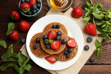 Tasty Dutch waffles (stroopwafels) with honey, berries and mint on wooden table, flat lay