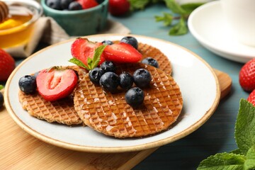 Tasty Dutch waffles (stroopwafels) with honey, berries and mint on light blue wooden table, closeup