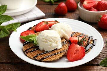 Tasty Dutch waffles (stroopwafels) with strawberries, ice cream and chocolate sauce on wooden table, closeup