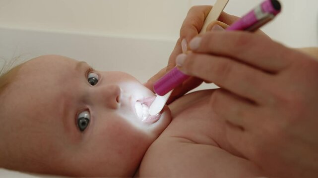A doctor examines a baby's mouth with a tongue depressor and a light, focusing on the child's health in a clinical setting. Doctor Examining Baby