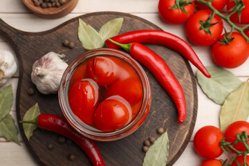 Tasty pickled tomatoes in jar and ingredients on wooden table, flat lay