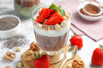 Delicious chocolate pudding with chia seeds, strawberries, yogurt and nuts in glass on white marble...