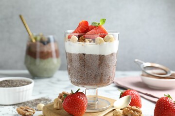 Delicious chocolate pudding with chia seeds, strawberries, yogurt and nuts in glass on white marble table, closeup