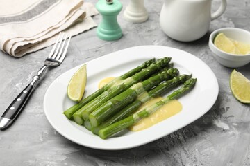 Tasty cooked asparagus served with sauce and lime on grey textured table, closeup