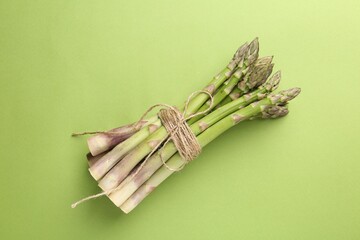 Tied raw asparagus on green background, top view