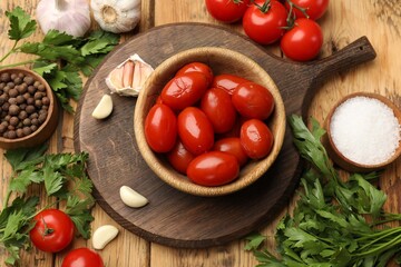 Tasty pickled tomatoes in bowl and ingredients on wooden table, flat lay