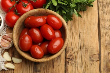 Tasty pickled tomatoes in bowl and ingredients on wooden table, flat lay. Space for text