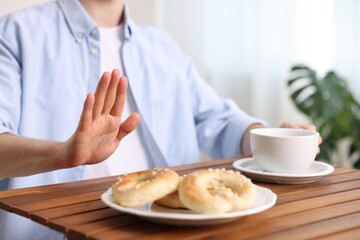 Gluten free diet. Man with cup of drink refusing from pastries at wooden table indoors, closeup