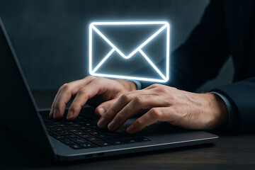 Typing on a laptop with a glowing email icon above the keyboard in a dark office environment setup