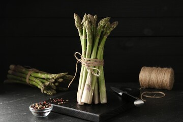Fresh raw asparagus spears and spices on black table