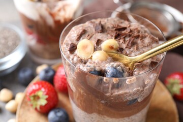 Taking delicious chocolate pudding with chia seeds, blueberries and hazelnuts from glass on table, closeup