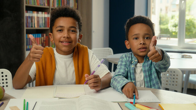 Happy little boys African American kids students pupils schoolboys friends siblings smiling children thumbs up gesture school primary education studying together writing desk classroom books learning