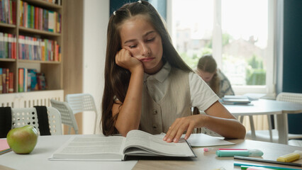 Bored schoolgirl Caucasian girl kid child pupil read book in school library sad tired learner student teenager upset frustrated boring lesson exhausted sleepy reading studying in classroom education