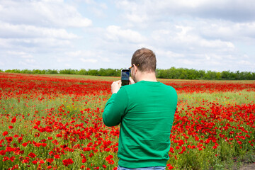 A Caucasian man in a verdant sweater captures the scarlet poppy sea under cotton-cloud skies on...