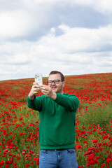 Joyful young Caucasian man captures selfie in vibrant poppy field; evoking Poppy Day, digital...