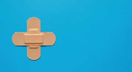 Obraz premium Two adhesive bandages forming a cross on a vibrant blue background. First aid and medical care concept. Minimalist horizontal flat lay layout.