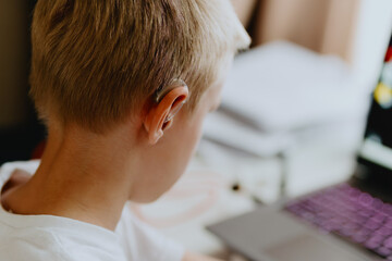 A boy with hearing aids enthusiastically plays computer games, showcasing inclusive play and...