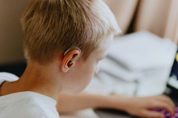 A boy with hearing aids enthusiastically plays computer games, showcasing inclusive play and...