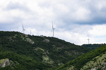 Mystical wind turbines crown verdant hills under brooding skies, invoking Tech Rebellion Day,...