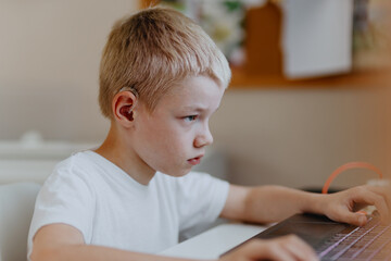 A boy with hearing aids enthusiastically plays computer games, showcasing inclusive play and...